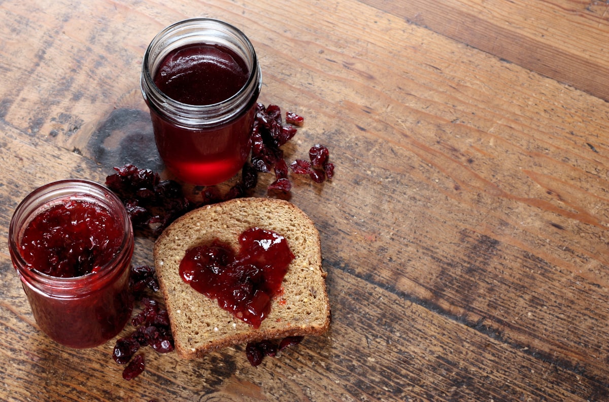 Zwei Gläser hausgemachte Konfitüre neben einer Scheibe Brot mit Marmeladenherz